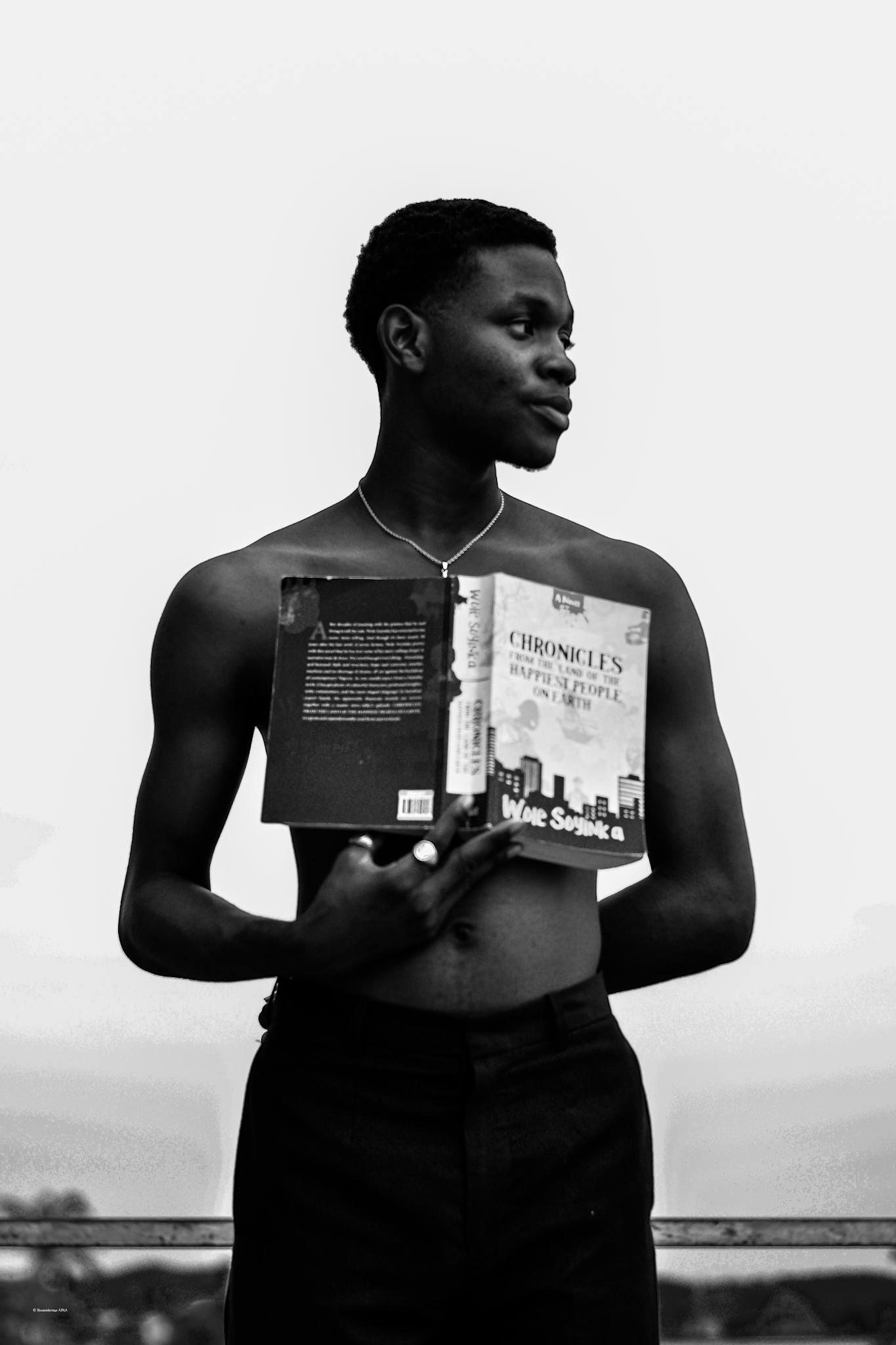 Artistic black and white portrait of a shirtless man holding an open book outdoors.